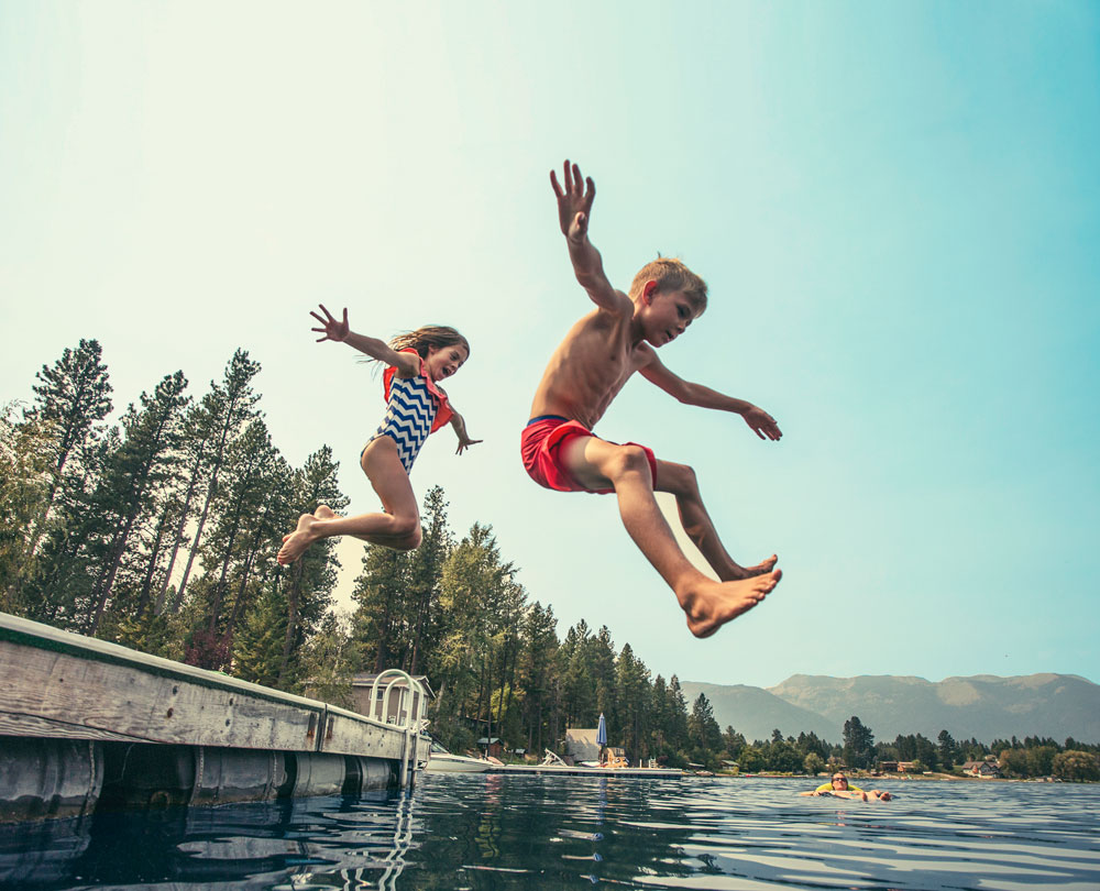 two kids jumping off a dock unto a lake