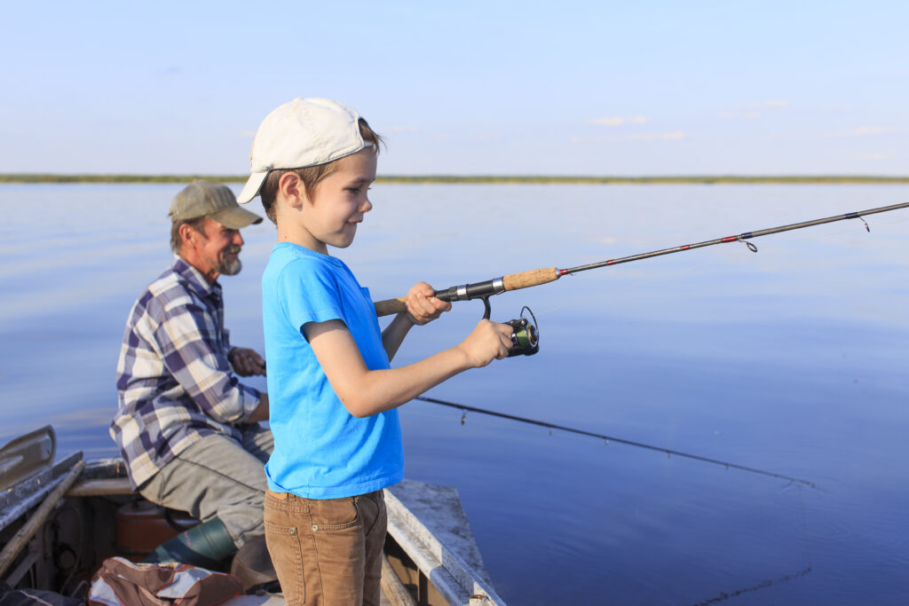 Grandfather and grandson fishing together on a spinning sitting in a boat on a river